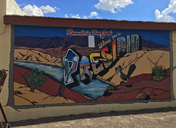 A photograph of a mural on the exterior of a building in west Texas. The mural, by Ramon G. Deanda, depicts the desert landscape with text that reads, "Panaderia Don José welcomes you to Presidio."