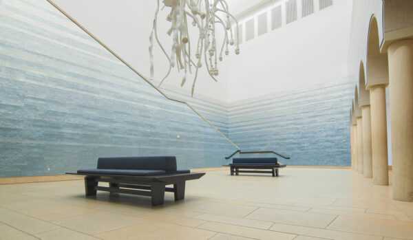 Photo of the main Atrium of the Blanton Museum of Art showing two site specific installations, one emulating a deep blue pool of water and another of a flora falling from the ceiling
