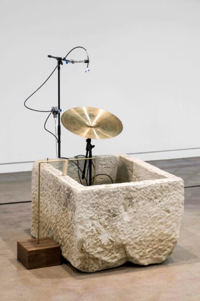 a sculpture of a symbol in a rock-like box, a bent aluminum pole, and a microphone