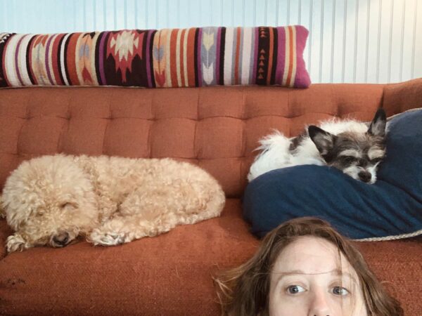 Artist Emily Peacock with her two dogs behind her asleep on an orange couch