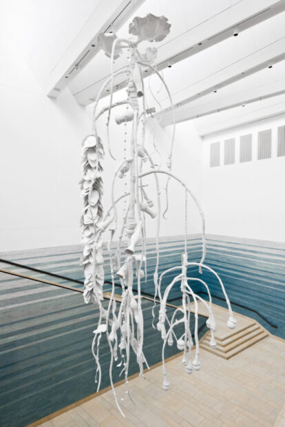A large, white, skeleton-like sculpture hangs from the ceiling of a two-story atrium.