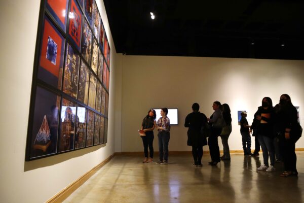 Image of visitors standing in a gallery space looking at objects on a wall at an opening