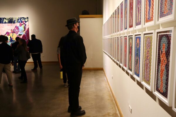 Image of a museum visitor looking at an installation of two dimensional objects on a wall at an exhibition opening