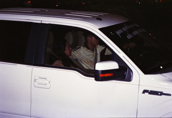 A photograph by Verónica Gaona of two people in a white SUV at nighttime.