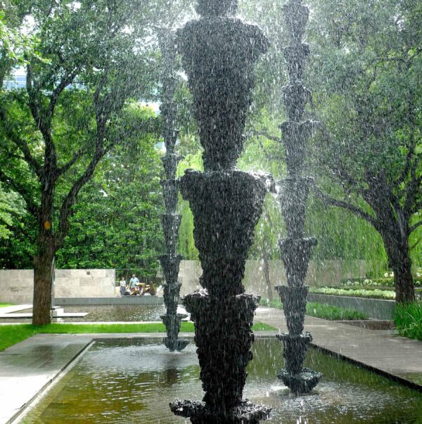 Detail of water pouring over three totem-like sculptures in a wading pool