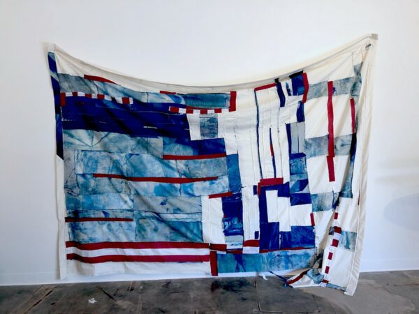 A detail of a fabric work by Alex Robinson using cut pieces of the US flag sewn together with cyanotypes on fabric.