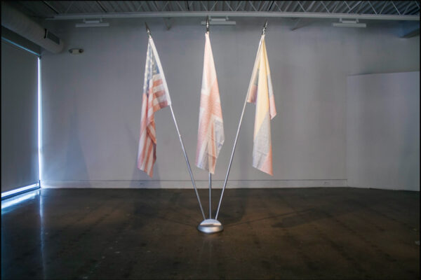 An installation by Bernardo Vallarino of three flags including a US flag which have been painted with a thin coat of white.