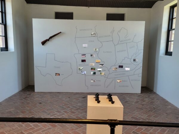 Installation photo of a map of midwestern and southern states drawn on a white wall with photos on various sites on different states