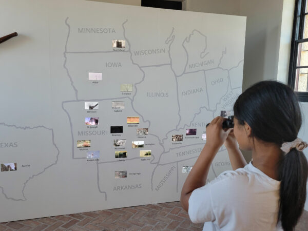 Photo of a child looking through a scope at a hand drawn map of the midwestern and southern United States with photos on various sites of different states