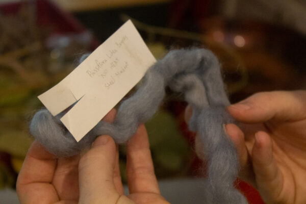 Two hands hold a tuft of dull blue fabric with a note attached that reads "Passifiora Lutea"