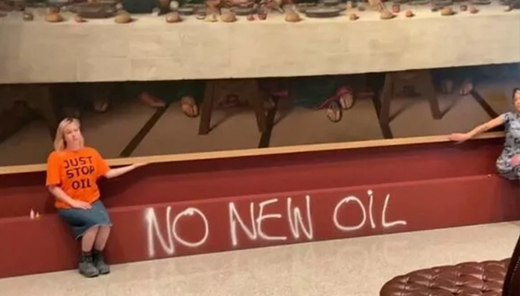 A person in an orange shirt sits with their hand on a painting's frame. The text "no new oil" is spray painted on the wall.