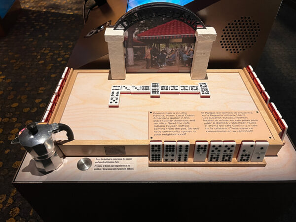 A sensory element in the Molina Family Latino Gallery . The object includes a set of dominoes in play and has a button that visitors can press to experience sounds and smells of Domino Park.