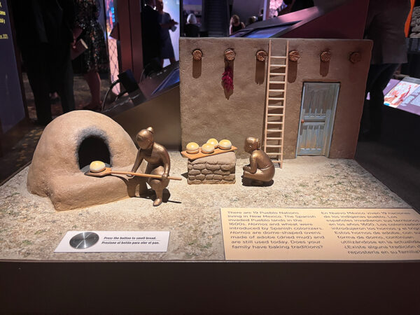 The diorama depicts two women baking bread using a dome-shaped oven. There is a button that visitors can press to smell the bread.