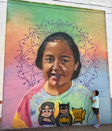 A photograph of Alithia Ramirez's mother standing next to a mural memorializing her.