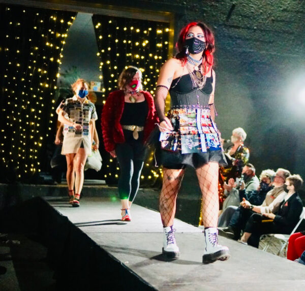 A photograph of three models walking down a runway featuring different looks that utilize reused materials.