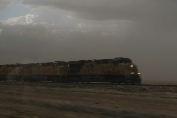 Fotografía borrosa de un tren en movimiento. Sus faros delanteros brillan contra un cielo gris. 