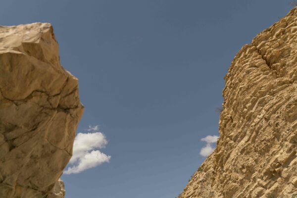 Fotografía contrapicada del cielo azul entre dos grandes piedras color ocre.