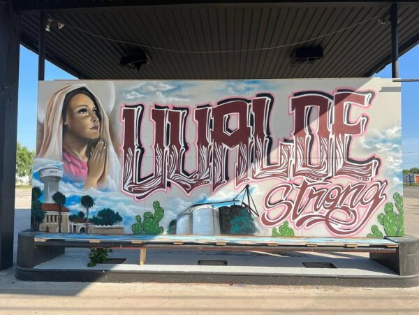A photograph of a mural painted by Cease Martinez and Alvaro “Deko” Zermeño. The mural shows a woman praying and images of the school with large text that reads, "Uvalde Strong."