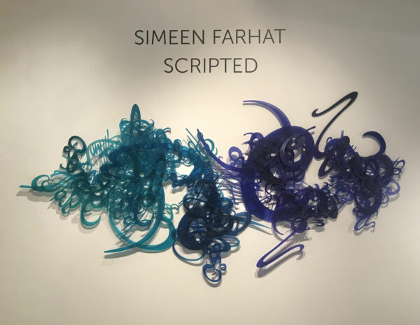 Installation photo of a wall sculpture of words and swirling patterns