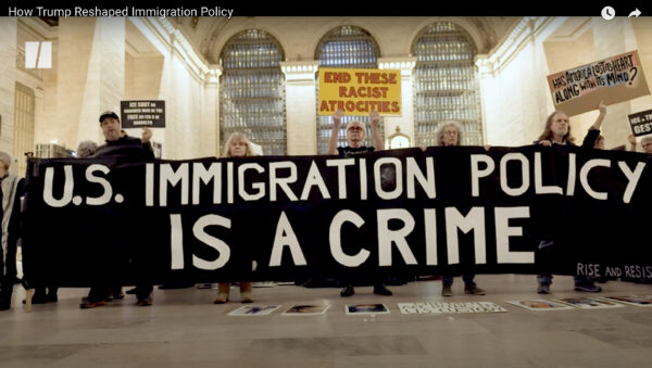 Photo of a protest with people holding a large sign that reads "U.S. Immigrations Policy is a Crime"