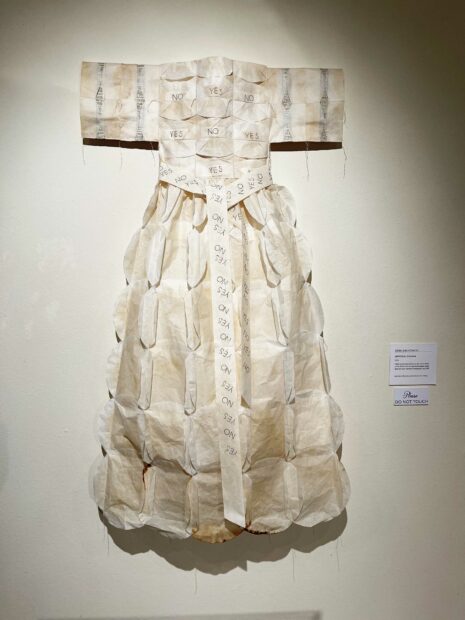 Installation of a female dress made of coffee filters hanging on a white wall