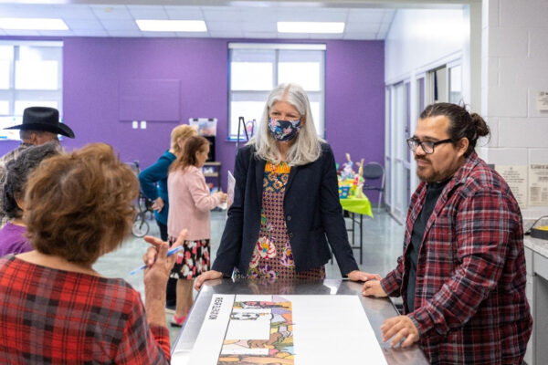 A photograph of artist David Maldonado standing at a table with Council Member Karla Cisneros and Denver Harbor community members. At the table they discuss a mural rendering by the artist.