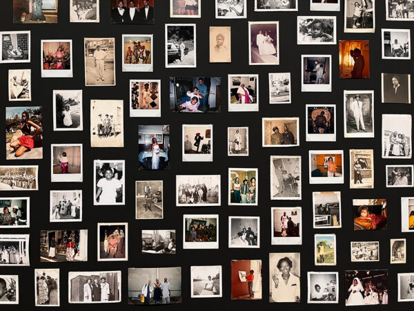 Sobre una pared negra cuelga una multitud de fotografías pequeñas, algunas a color y otras en blanco y negro. 