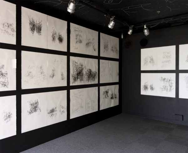 Installation view of works on paper on a black wall