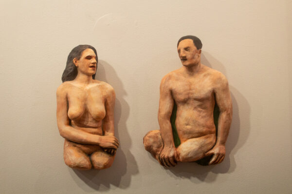 Two painted ceramic wall sculptures feature a nude man and a nude women seated across from each other
