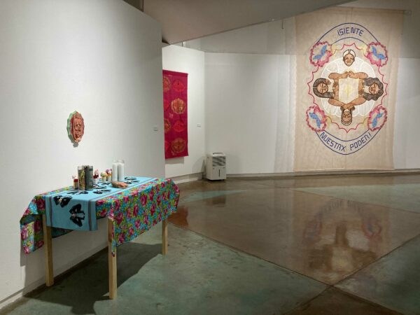 Exhibition view with an ofrenda table on the left and a large tapestry on the rightr