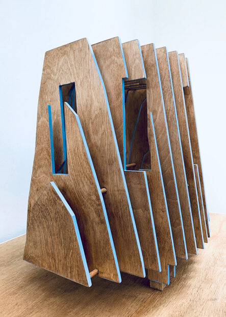 A tall wooden sculpture made from thin panels of wood with blue-painted edges.
