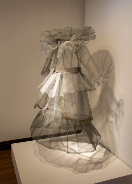 A gown with a full skirt is made out of mesh and sits on a white plinth