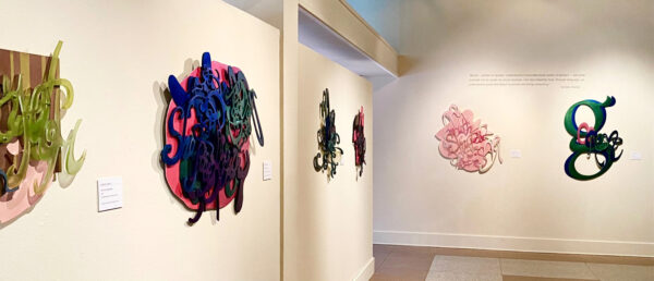 installation view of two dimensional sculptures of words and letters on a white wall