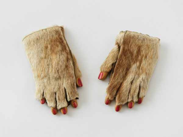 A sculpture comprised of two fur-covered gloves, all of which have fingers with red painted nails.