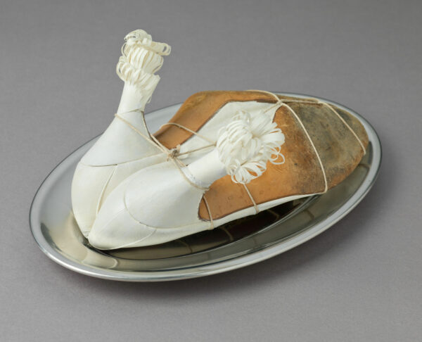 A sculpture comprised of a pair of high heels, turned upside-down and tied together. The stilettos each have turkey frills on the high heels.
