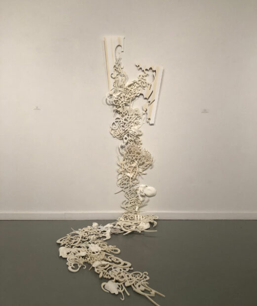 White sculpture of words and letters cascading down from a wall