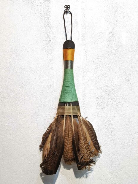 Talisman sculpture of colored string and feathers hanging on a white wall