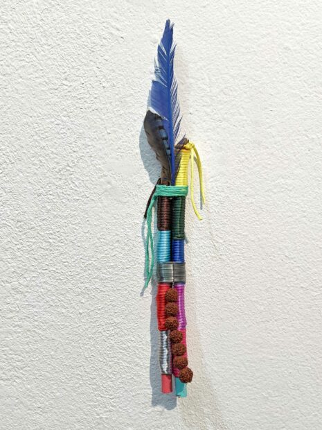 Talisman sculpture of colored string and feathers hanging on a white wall