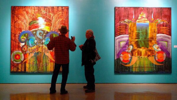 Photo of two individuals in front of two large scale paintings on a turquoise wall