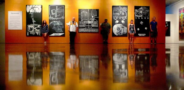 Installation photo of five black and white drawings with visitors standing in front of them