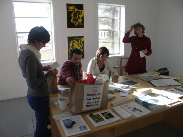 A photograph of an intern in an office with three other people The group prepares membership bags. 