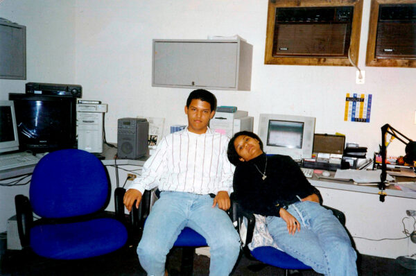 A 1997 photograph of two young people sitting in office chairs at a computer workstation. 