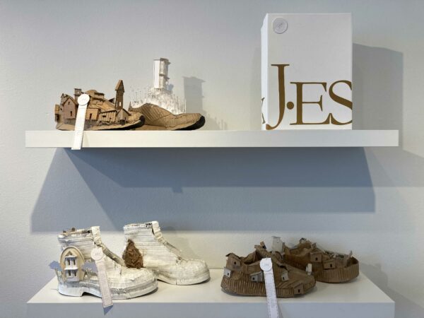 Installation view of shoes built to look like a city made from cardboard sitting on a shelf