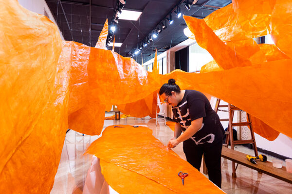 Artist Justin Favela works with large sheets of orange tissue paper as he installs his new work "Revoloteo."