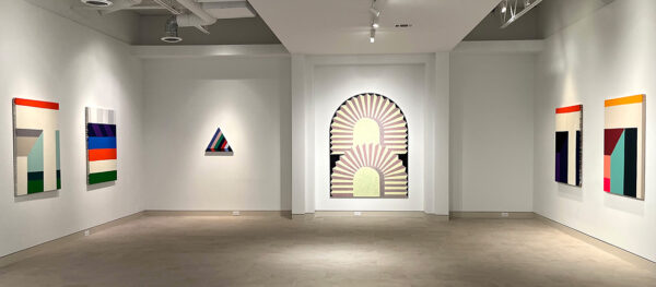 An installation image of large scale geometric paintings installed in a white-walled gallery.