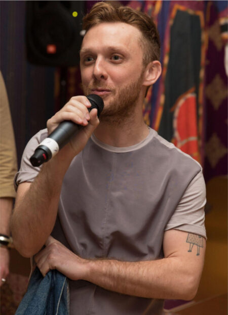 A photograph of Danny Orendorff. He holds a microphone in one hand and looks off into the the distance as he addresses an unseen crowd.