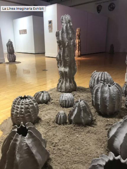 An installation by Karla García featuring an array of clay cacti sculptures sitting on a mound of dirt inside a gallery.