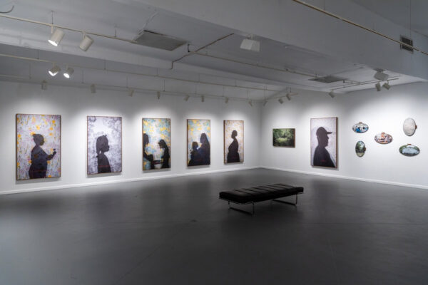 Installation photograph of a gallery, featuring artworks installed on the walls. In the art, there are silhouettes of people.