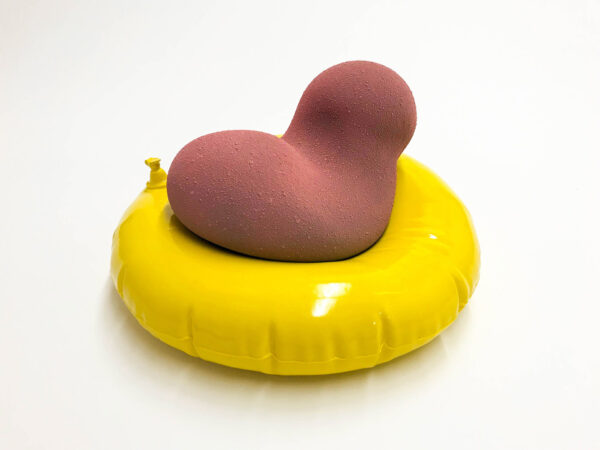 A sculpture by Nate Ditzler depicting an amorphous lightly textured coral color object placed on top of a yellow inflatable inner tube.