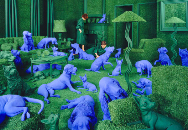A photograph of an all-green room, with two people in the background. Most of the room is occupied by resin-cast deeply blue-colored dogs.